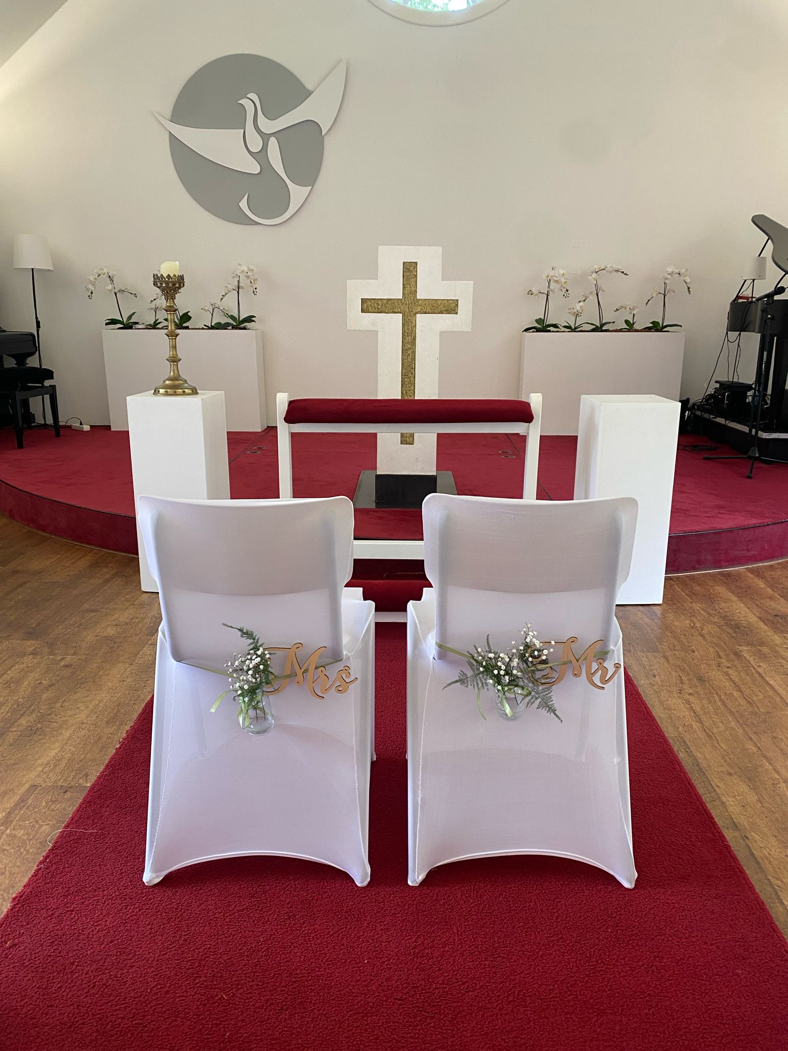 Twee witte stoelen met Mr en Mrs borden en bloemvaasjes voor het altaar op de rode loper