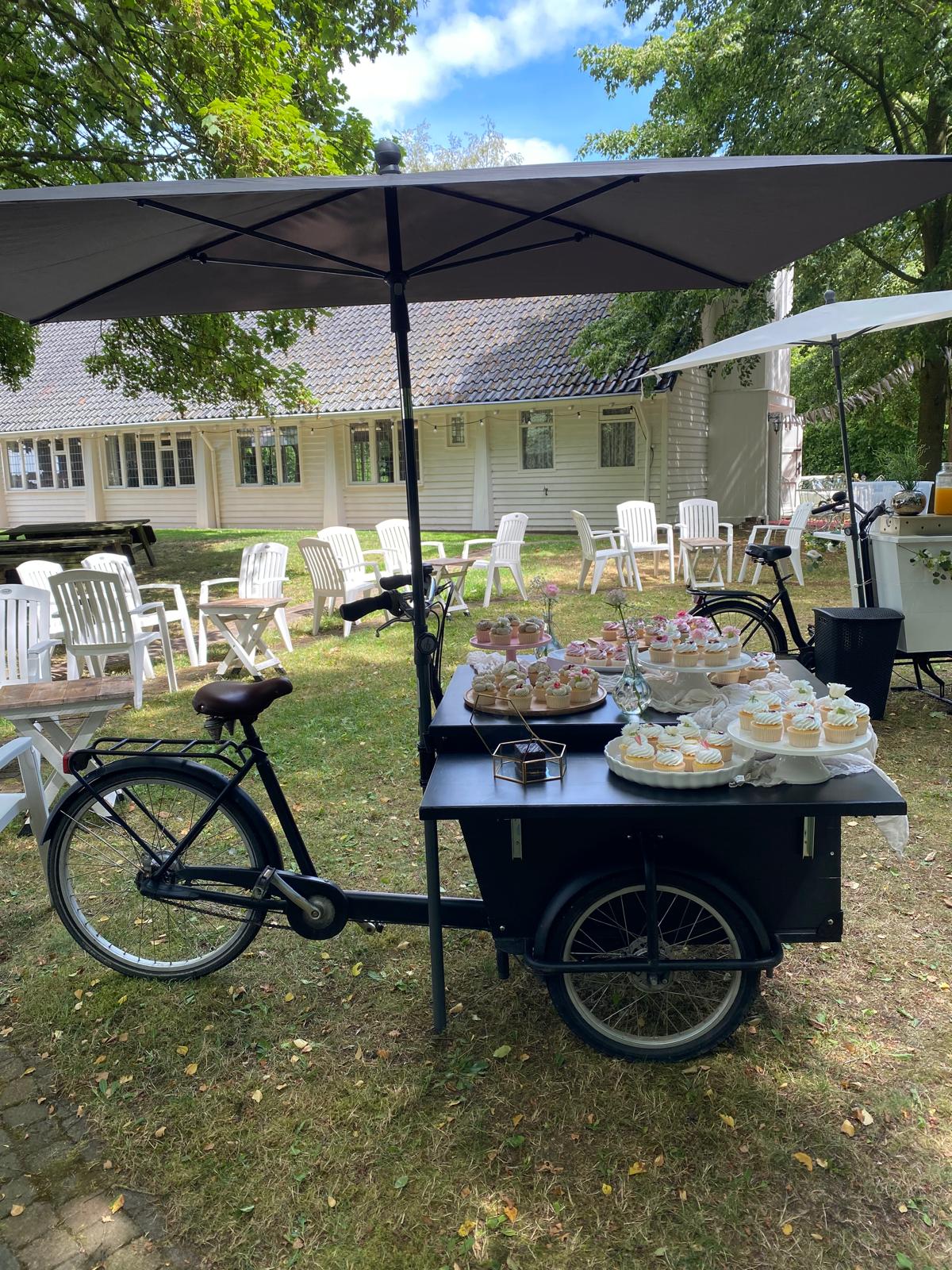 Foodbike met etagères vol cupcakes en zoete lekkernijen onder een parasol in de tuin