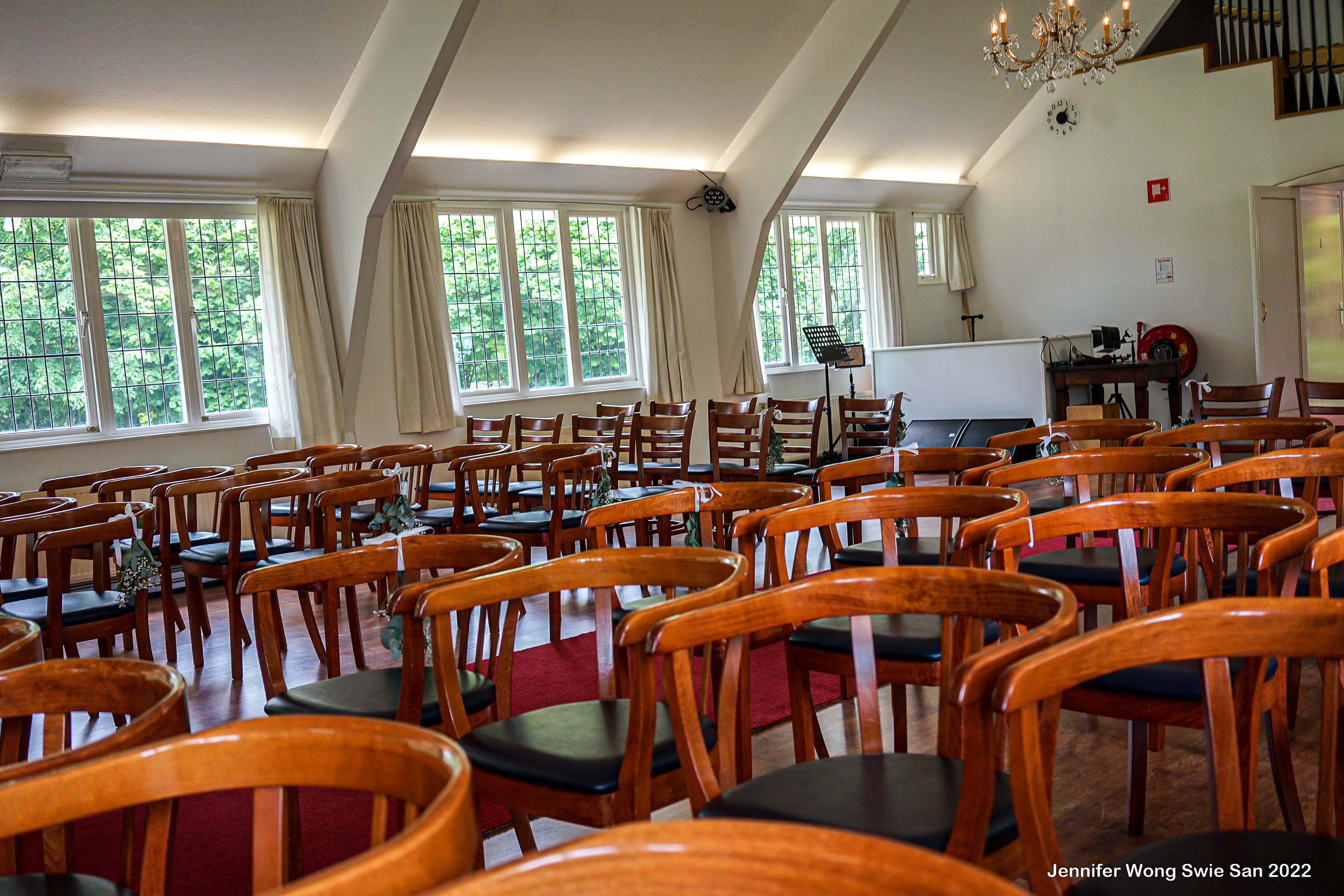 Ceremonie-zaal symmetrisch richting het altaar: drie kristallen kroonluchters, groot roosvenster en rijen stoelen