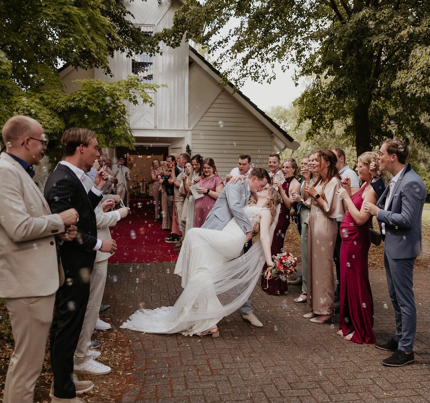 Bruidspaar kust elkaar bij het uittreden terwijl gasten bellen blazen voor het Wit Kerkje